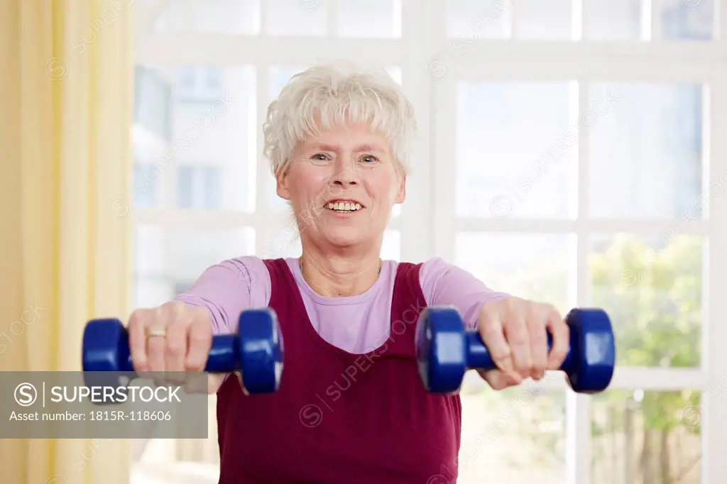 Germany, Duesseldorf, Senior woman exercising with barbell, smiling