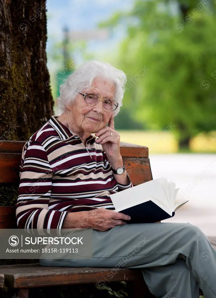 Austria, Senior woman sitting on bench and reading book