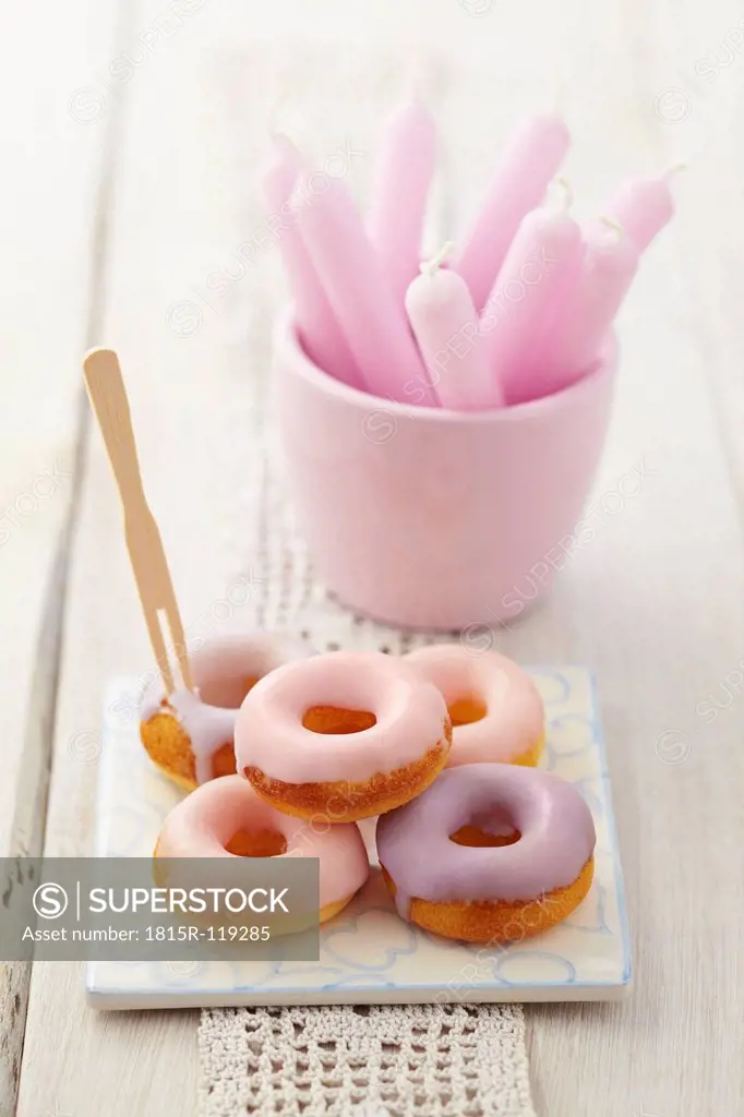 Glazed baked doughnuts on tile with candles in glass