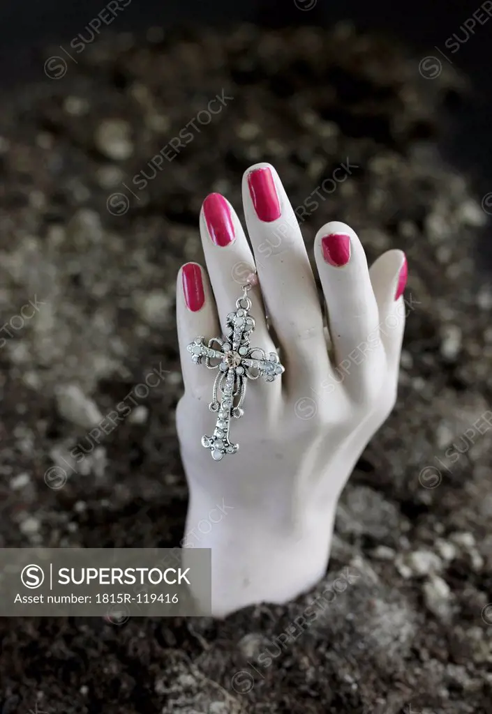 Human hand of mannequin with crucifix in soil at cemetery