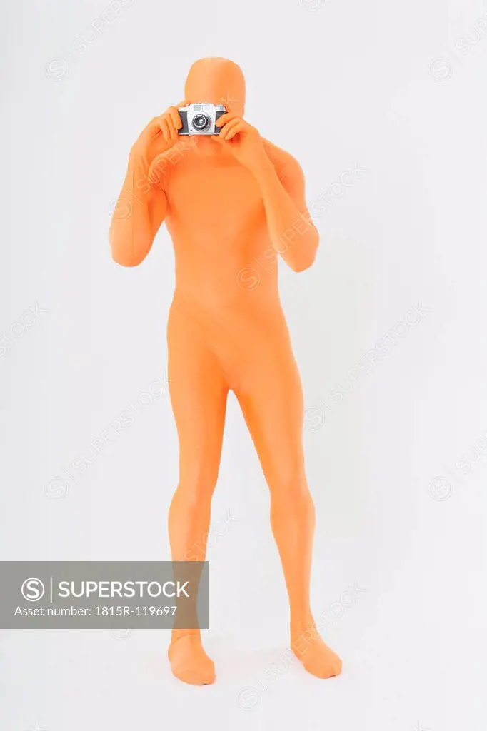 Mature man in orange zentai with camera standing on white background