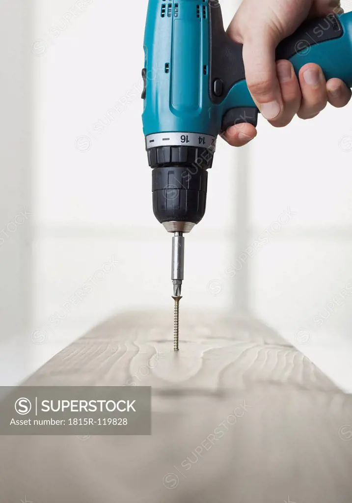 Human hand driving screw into wooden board with power drill