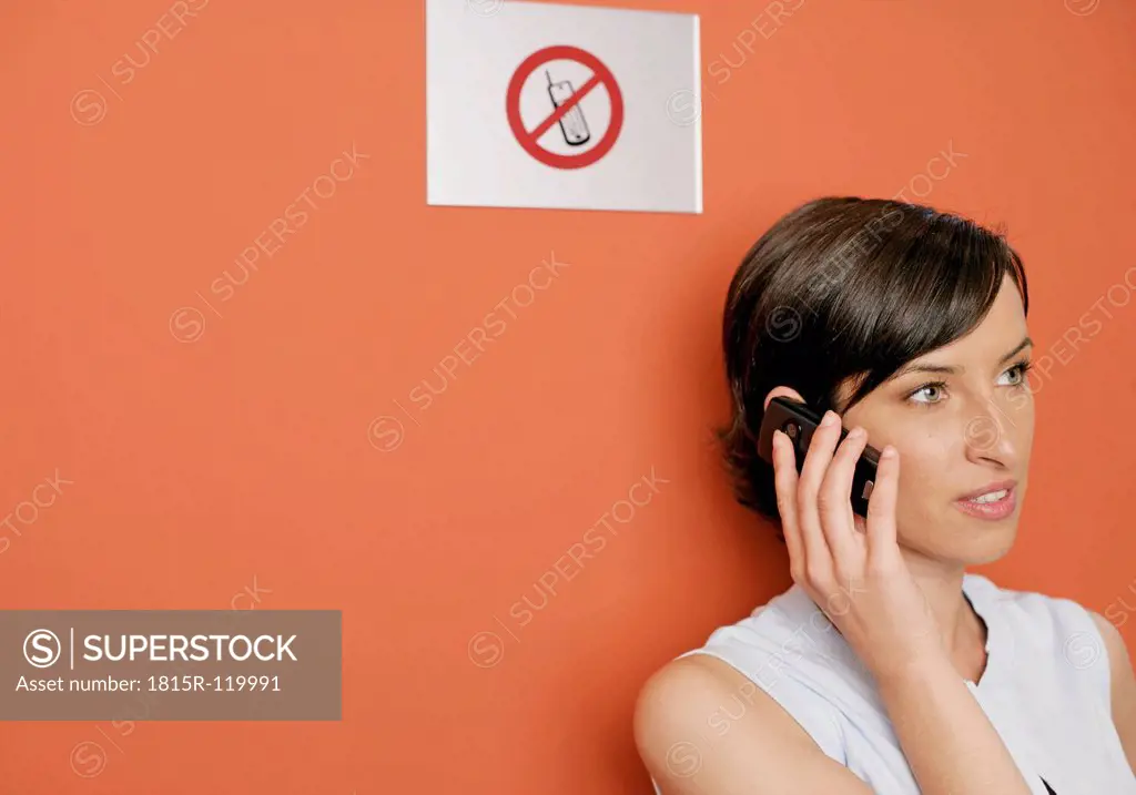Young woman talking on cell phone in front of sign, close up