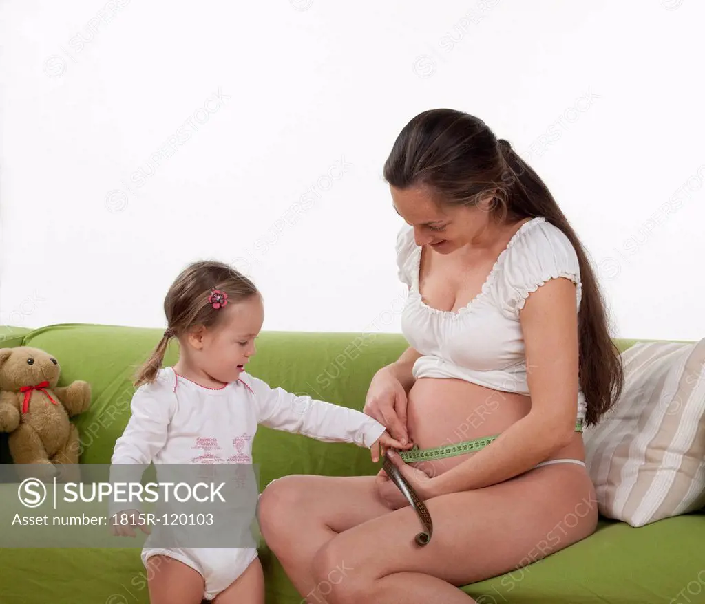 Pregnant woman measuring abdominal girth while daughter looking at her
