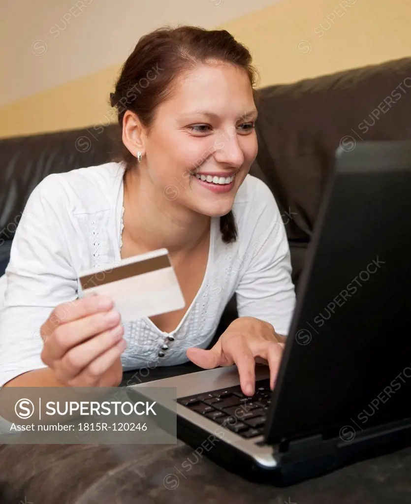 Germany, Brandenburg, Young woman shopping online from home with laptop and credit card