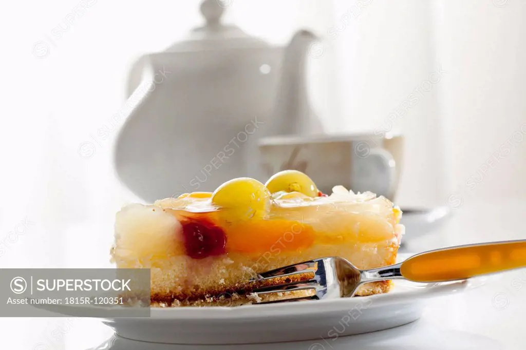 Plate of fruit tart cake and tea pot with cup in background, close up