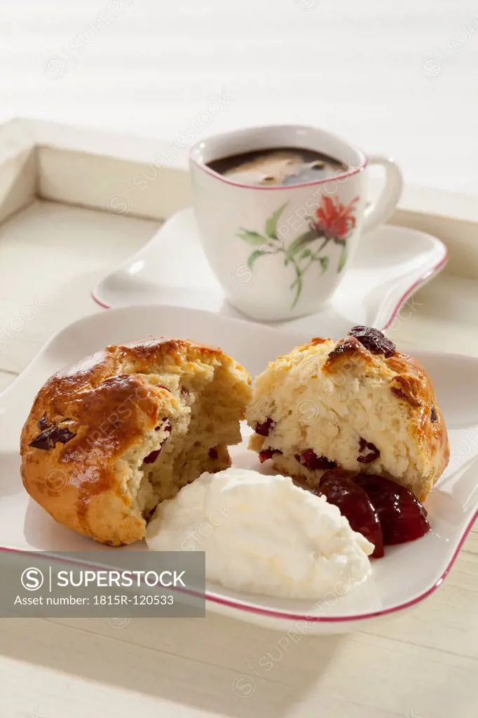 Cranberry scones with whipped cream and cup of coffee in tray, close up