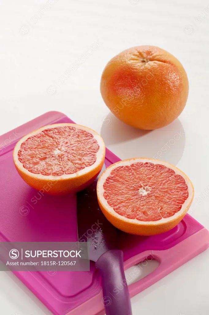 Grapefruit with chopping board and knife on white background, close up