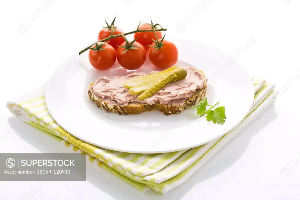 Liverwurst and gherkin on whole grain bread besides tomatoes, close up