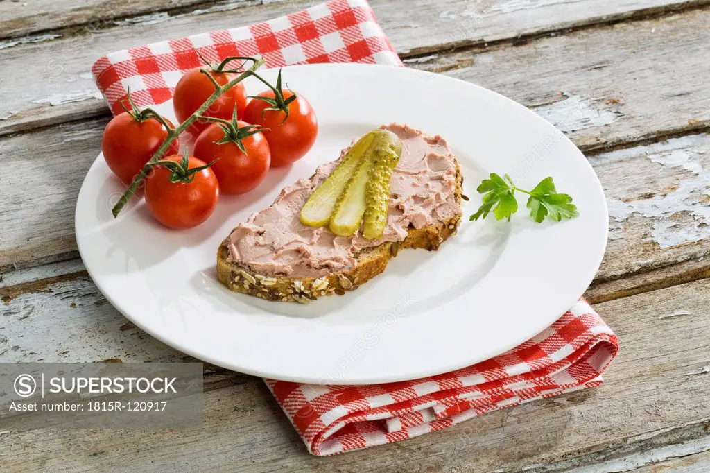 Liverwurst and pickle on whole grain bread besides tomatoes, close up