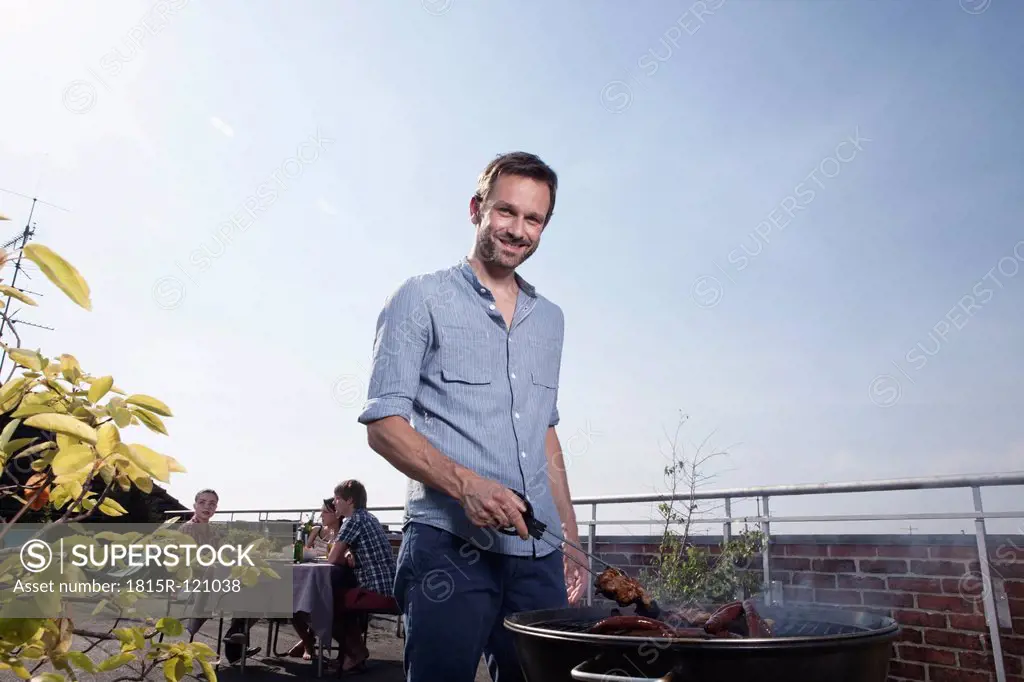 Germany, Berlin, Portrait of man barbecueing on grill, smiling