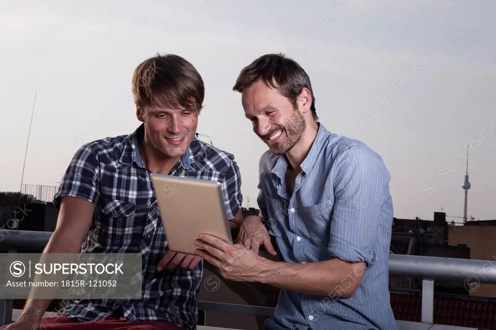 Germany, Berlin, Men with digital tablet on roof terrace, smiling