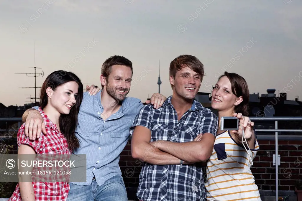 Germany, Berlin, Group of friends taking self photograph on roof terrace, smiling