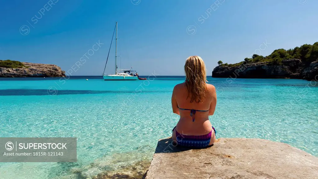 Spain, Menorca, Woman sitting on jetty at Cala Turqueta