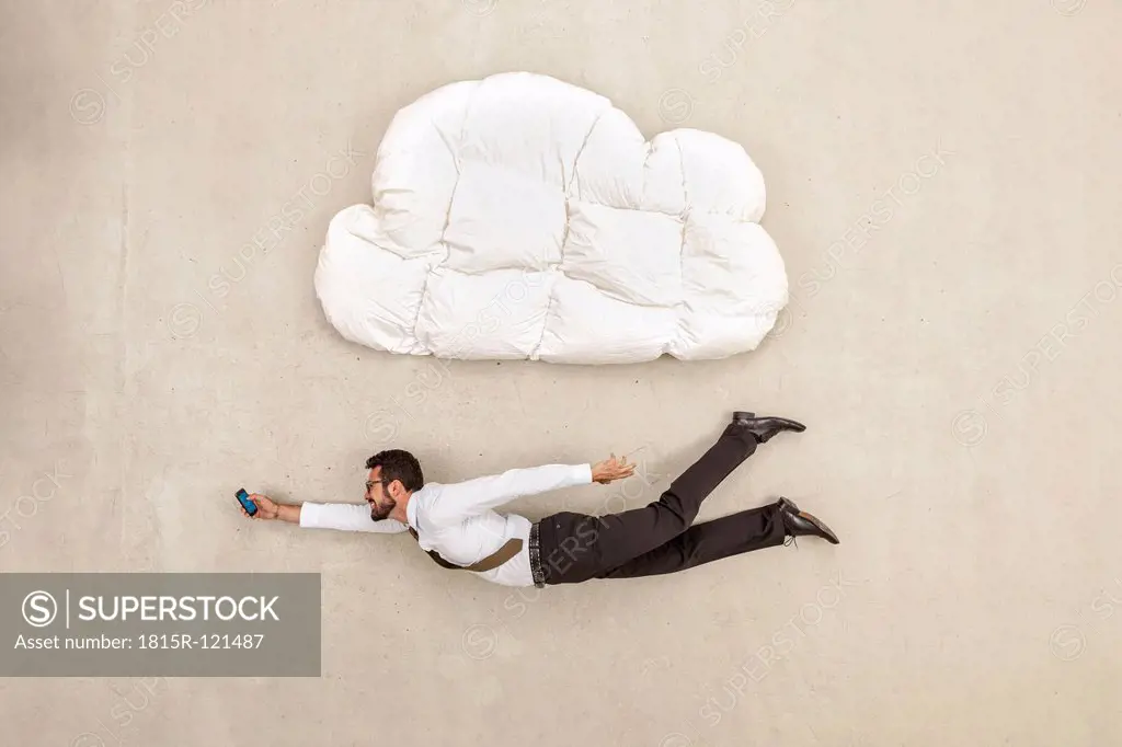 Businessman holding mobile phone and flying below cloud shape pillow
