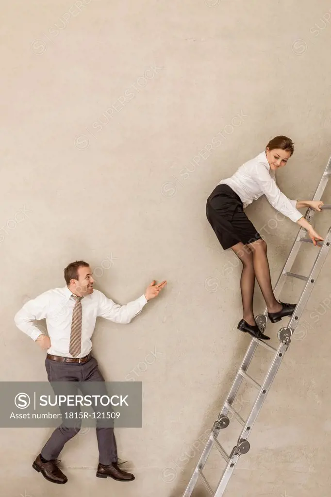 Businessman teasing while businesswoman climbing ladder in office