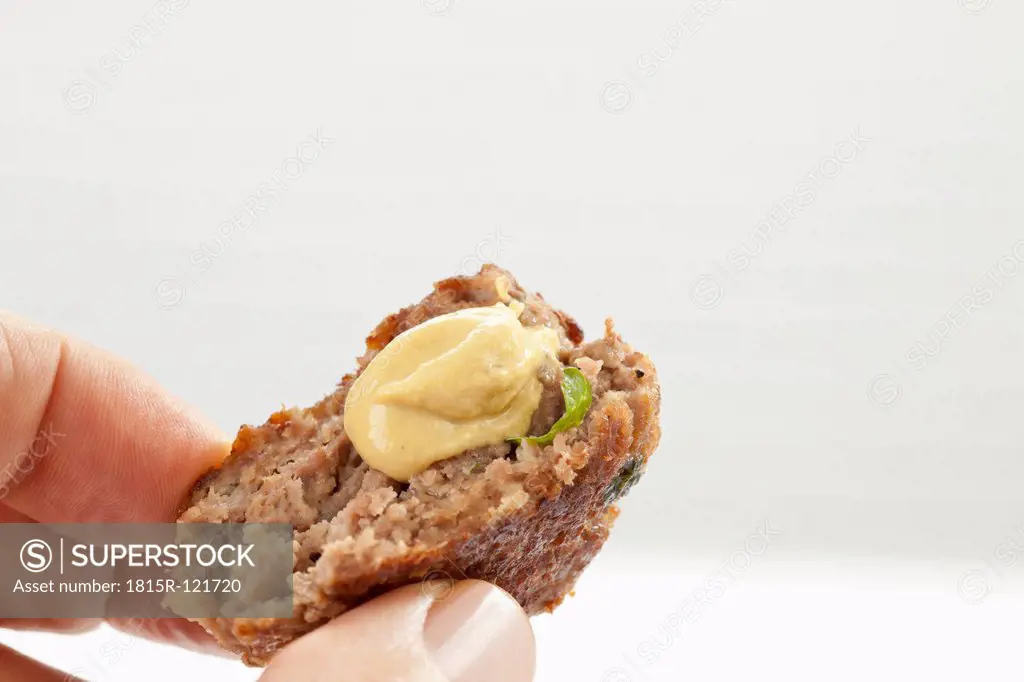 Human finger holding fried minced pork patties with mustard, close up