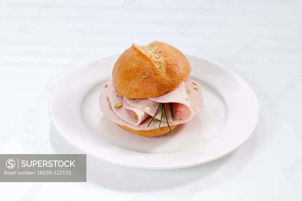 Sandwich of bread roll with mortadella and pistachio on plate, close up