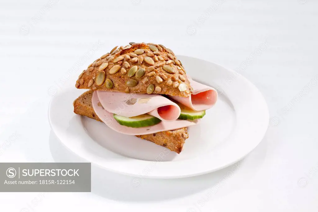 Sandwich of whole grain bread roll with mortadella and mushrooms on plate, close up