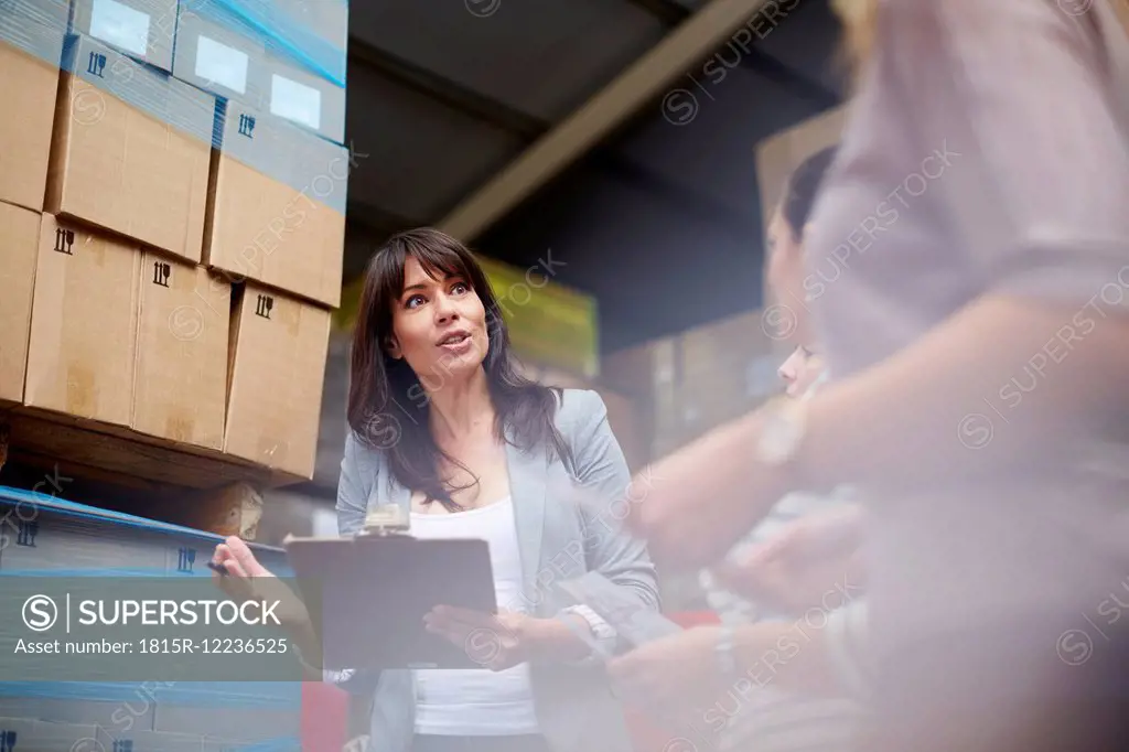 Woman with clipboard in warehouse talking to women