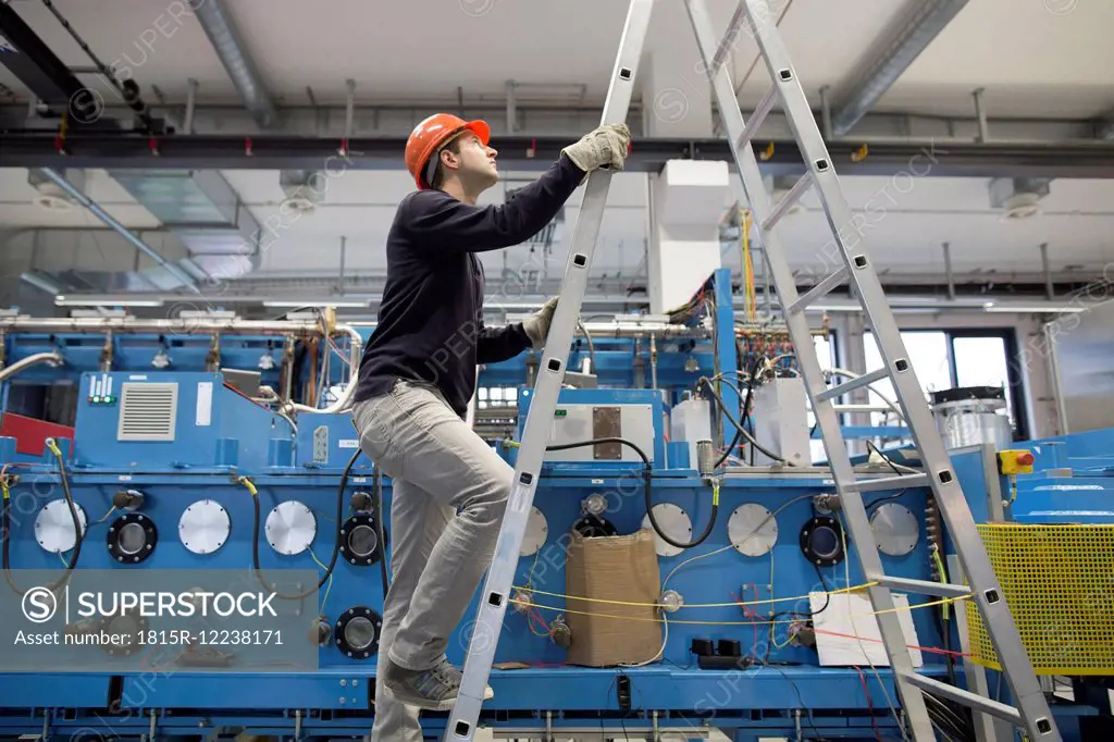 Young technician climbing up a ladder in an industrial hall