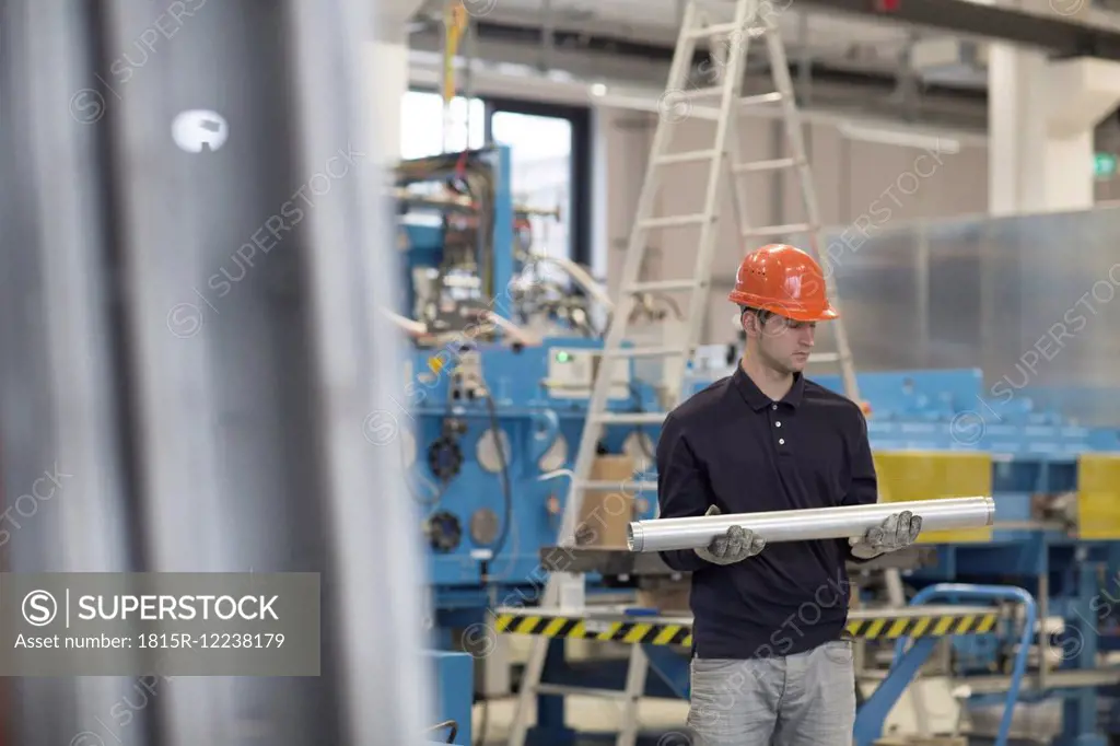 Young technician carrying pipes at industrial hall