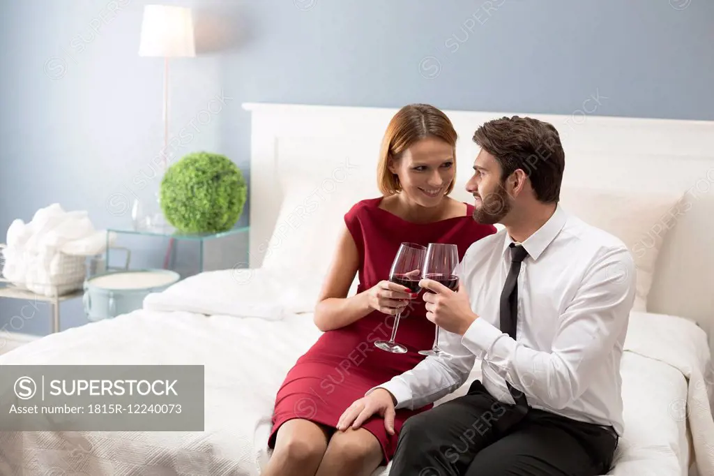 Affectionate couple holding wine glasses in bedroom