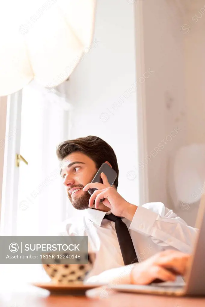 Businessman with laptop and cup of coffee on cell phone