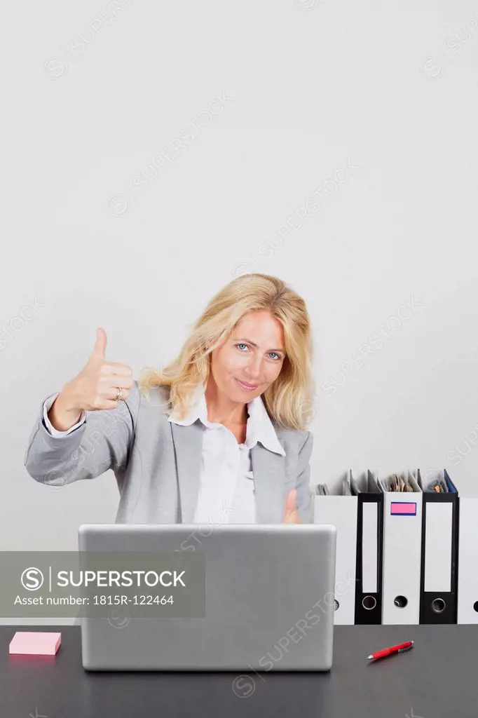 Portrait of businesswoman using laptop and showing thumbs up, smiling