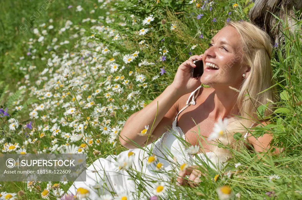 Austria, Salzburg, Mid adult woman talking on cell phone in meadow, smiling