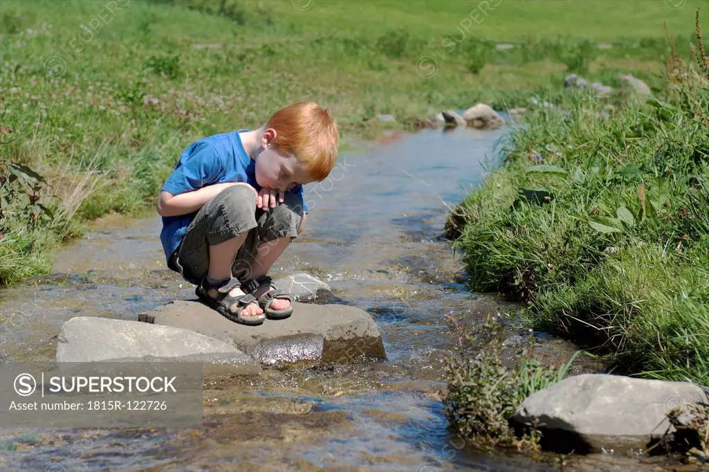 Germany, Bavaria, Boy sitting on rock at brook