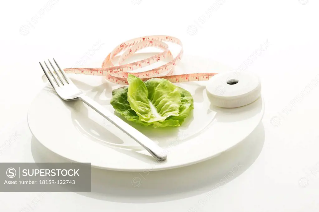 Lettuce leaf with fork and measuring tape on plate, close up