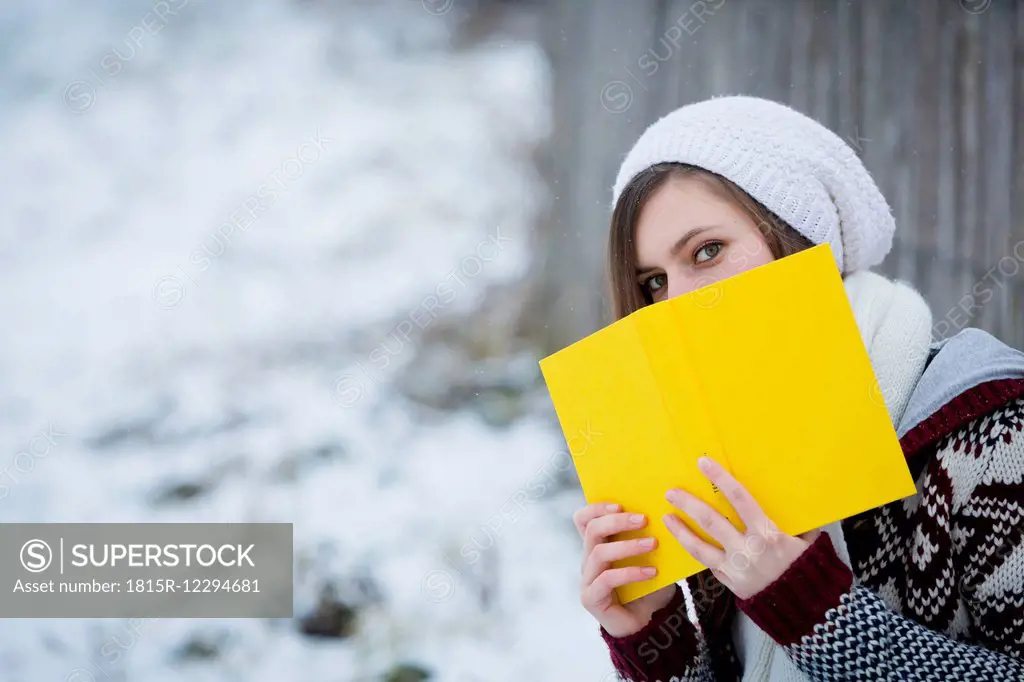 Young woman hiding behind yellow book