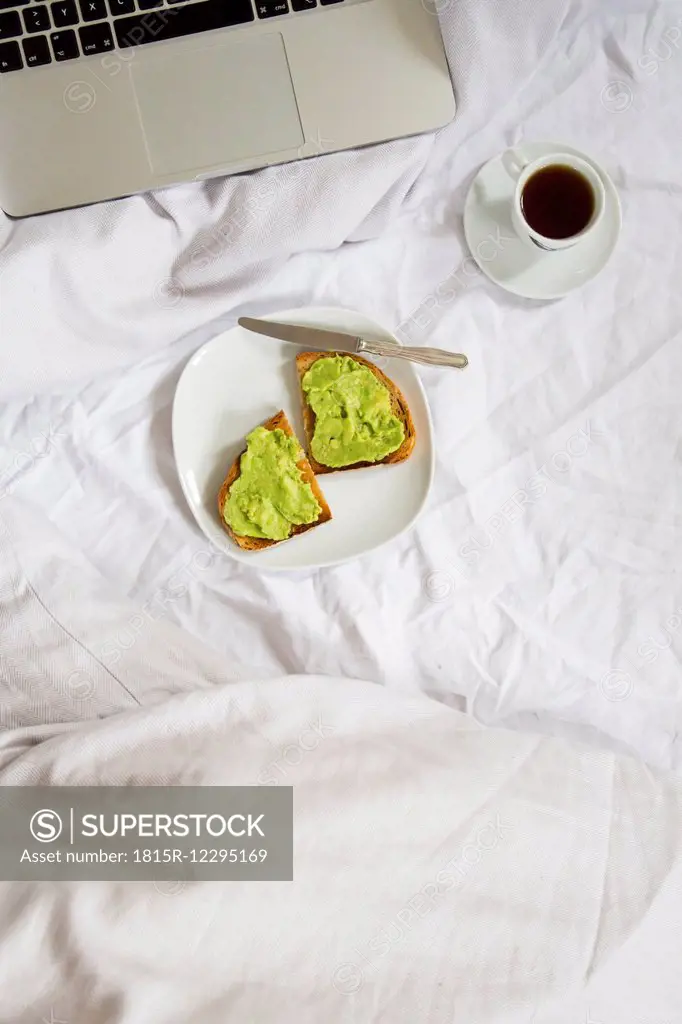 Bread with avocado cream and cup of coffee next to laptop