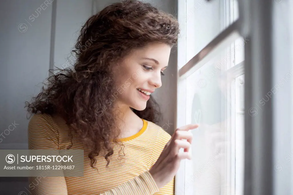 Smiling young woman painting heart on windowpane