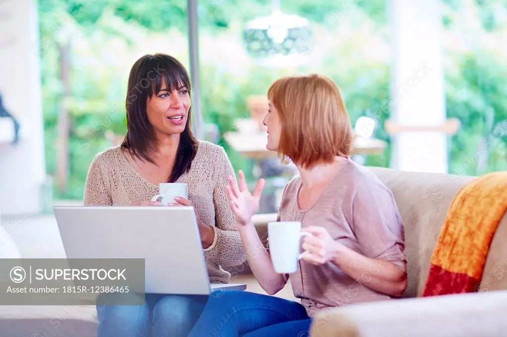 Two women sitting on couch with laptop and cups