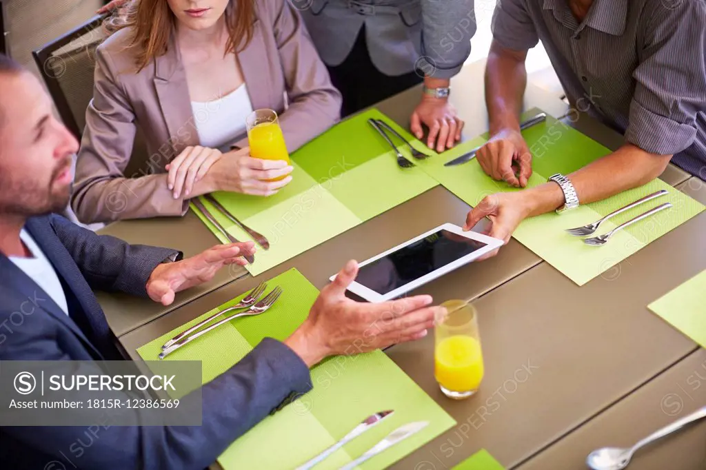 Businessman showing digital tablet to colleagues at dining table