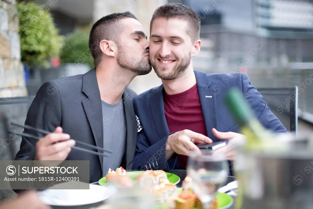 Gay couple kissing and eating sushi at outdoor restaurant