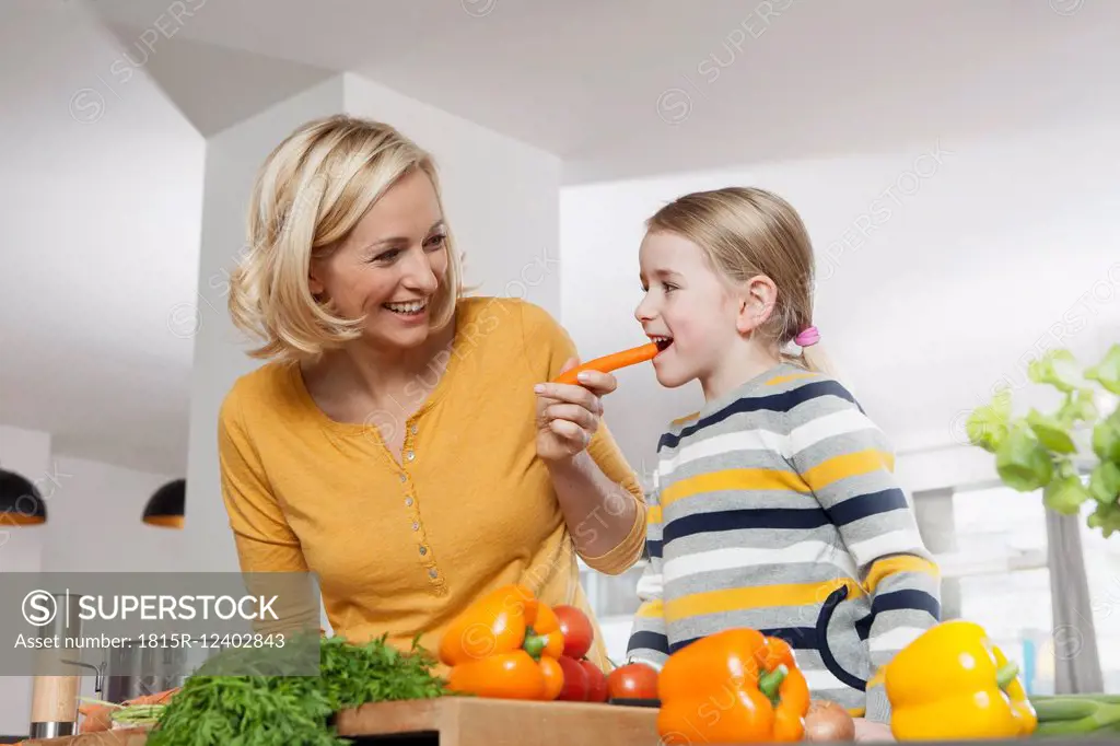 Mother with daughter eating carrot in kitchen