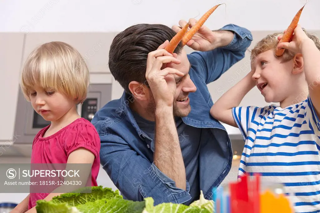 Father playin with kids in kitchen, making carrot horns