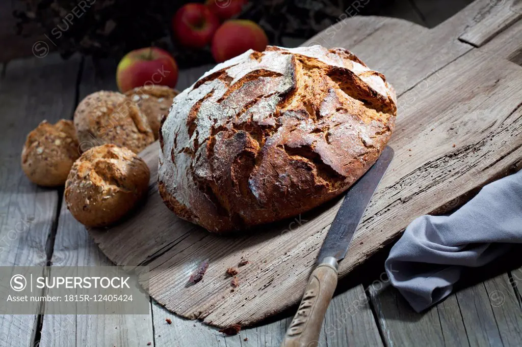 Crusty bread and old bread knife on chopping board, granary rolls
