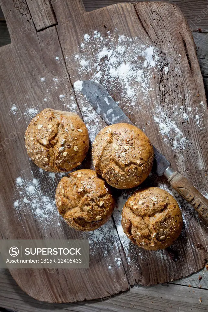 Wholemeal bread rolls, old bread knife and flour on wooden chopping board