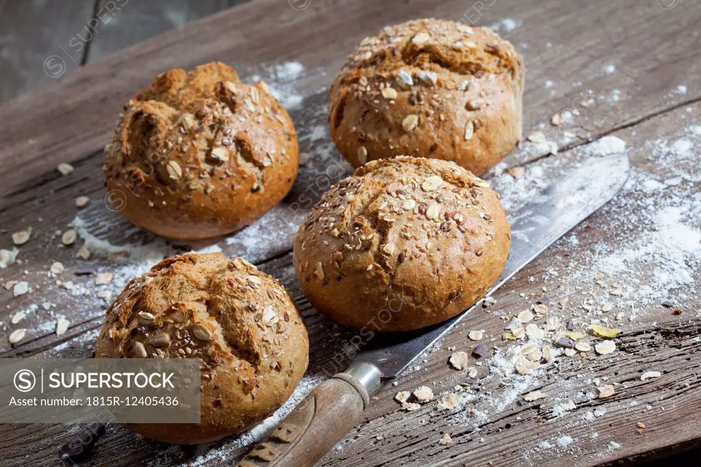 Wholemeal bread rolls, flour and old bread knife on wood