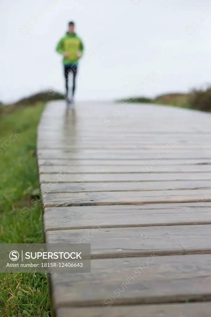 Spain, Valdovino, defocused man running on a boardwalk at a rainy day