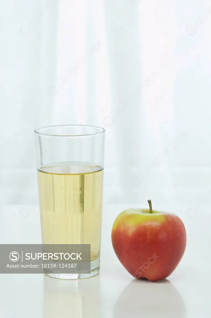 Glass of apple juice beside apple on table against white background, close up