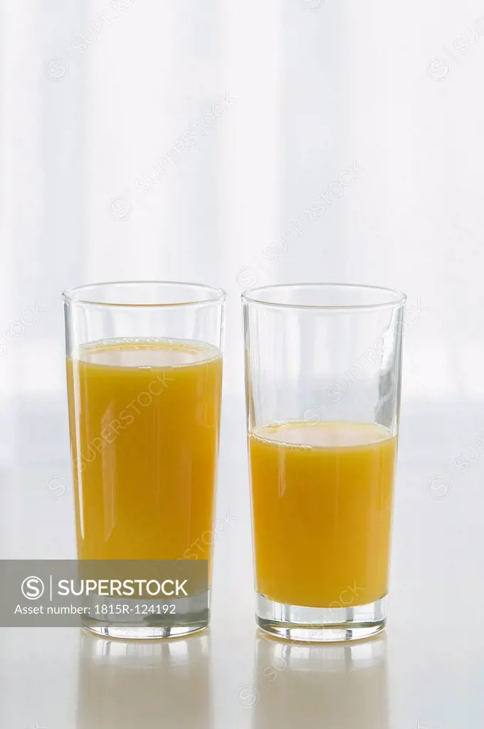 Glasses of orange juice on table against white background, close up