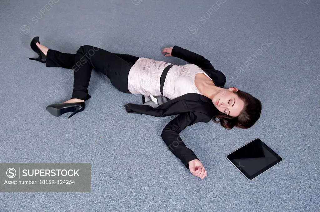 Germany, Berlin, Exhausted businesswoman lying on floor beside digital tablet