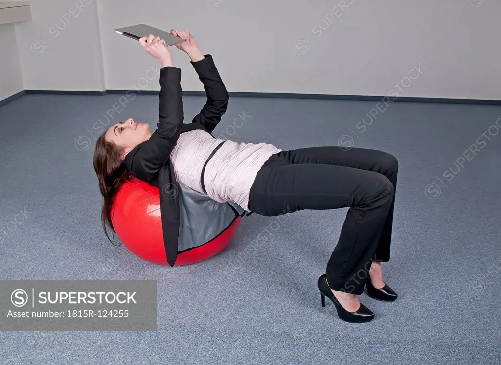 Germany, Berlin, Businesswoman bending over exercise ball with digital tablet
