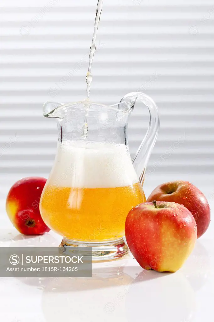 Apple juice being poured into pitcher besides apples