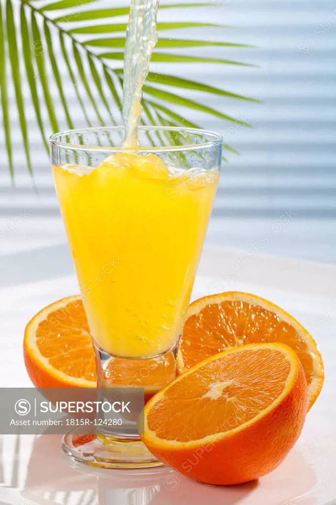 Orange lemonade being poured into glass besides oranges, close up